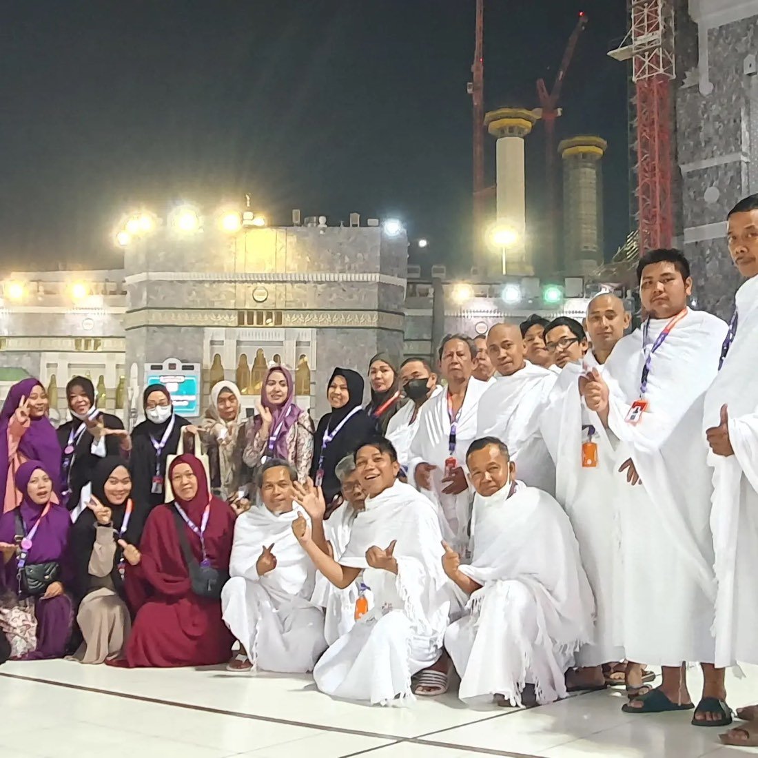 Rombongan jamaah berihram putih berfoto di pelataran Masjidil Haram pada malam hari